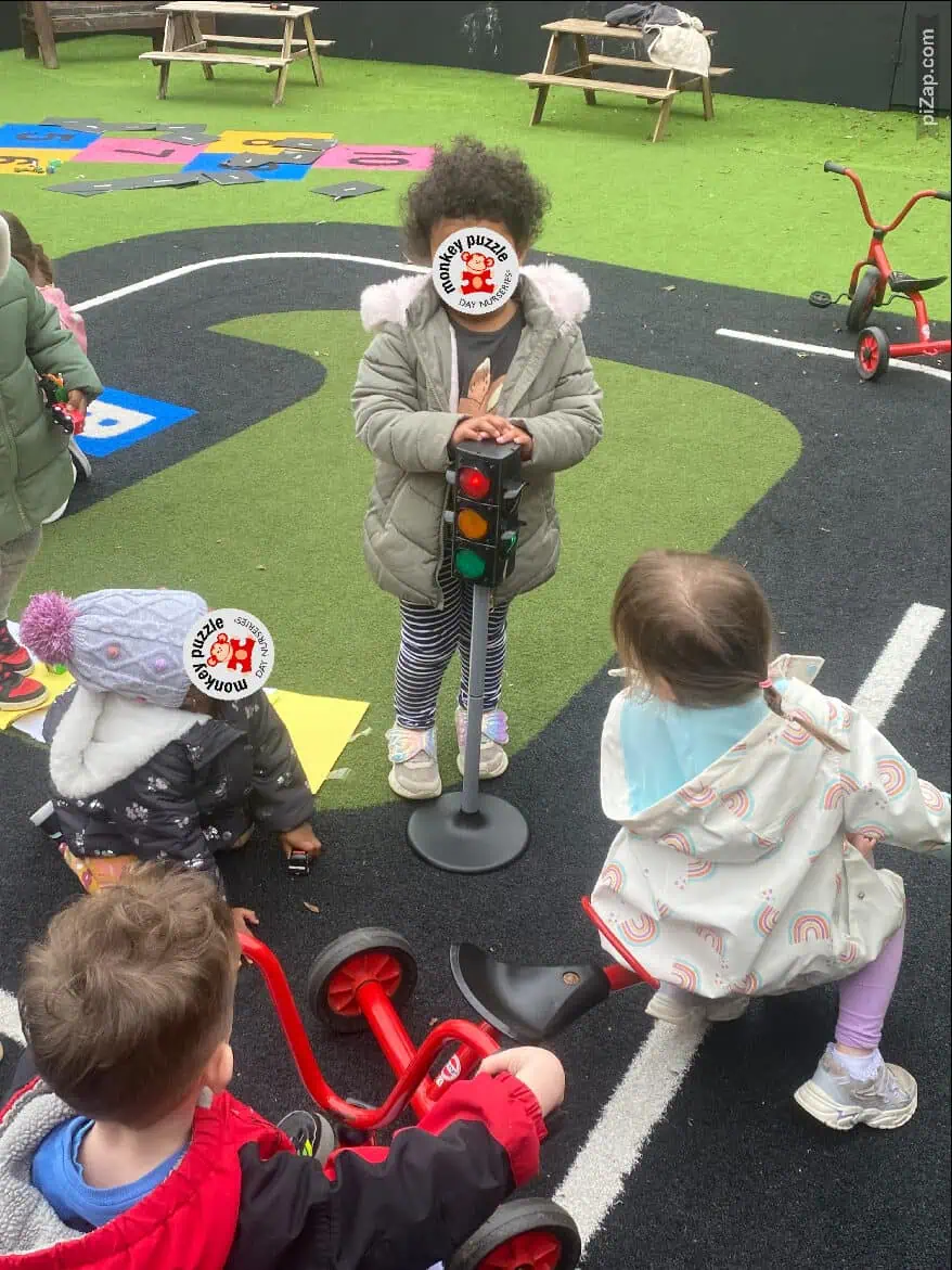 Colorful preschool outdoor play area at Monkey Puzzle Day Nursery Enfield, children engaged in educational activity with traffic lights and riding toys, ideal for early childhood development and learning.